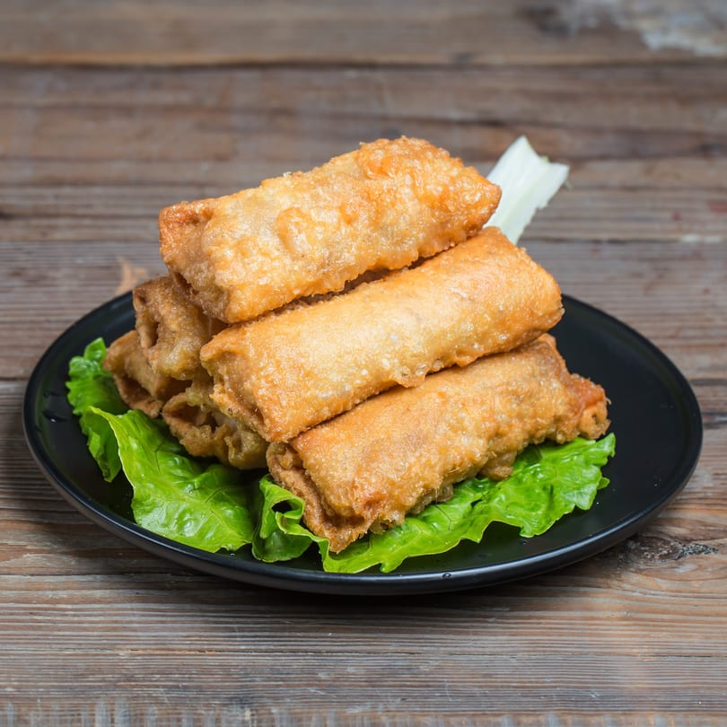 Crispy golden-brown Thai spring rolls, stacked on a black plate with fresh green lettuce.