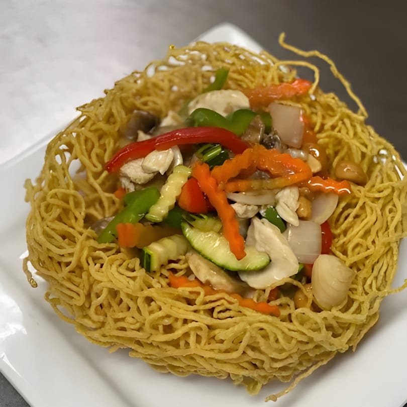 Crispy Thai noodles forming a bowl, filled with chicken, colorful vegetables, and a savory sauce.